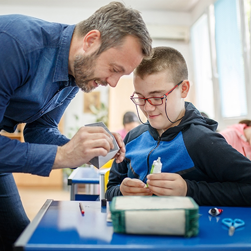 A photographic style image of a special education teacher helping a student.